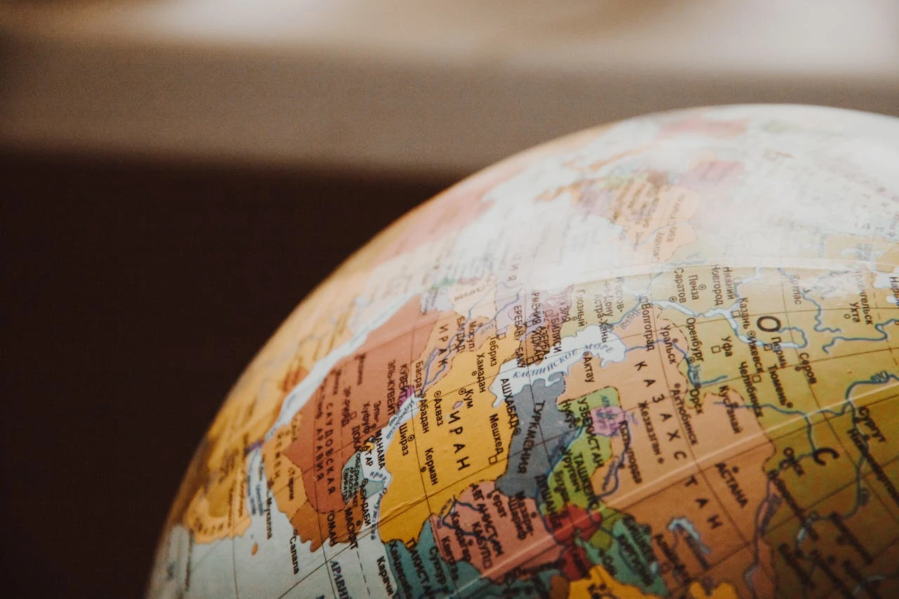 A close-up photograph of a globe focused on a portion of North America, showing part of Canada, Mexico, and the United States. The image is shot at an angle, creating a curved perspective of the geographical boundaries. The colors are muted and warm, with countries shown in different pastel shades of orange, yellow, and pink. The globe appears to be illuminated, giving it a soft, educational quality. The background is dark and blurred, making the map details stand out.