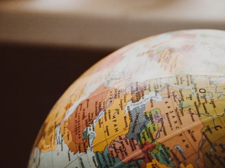 A close-up photograph of a globe focused on a portion of North America, showing part of Canada, Mexico, and the United States. The image is shot at an angle, creating a curved perspective of the geographical boundaries. The colors are muted and warm, with countries shown in different pastel shades of orange, yellow, and pink. The globe appears to be illuminated, giving it a soft, educational quality. The background is dark and blurred, making the map details stand out.